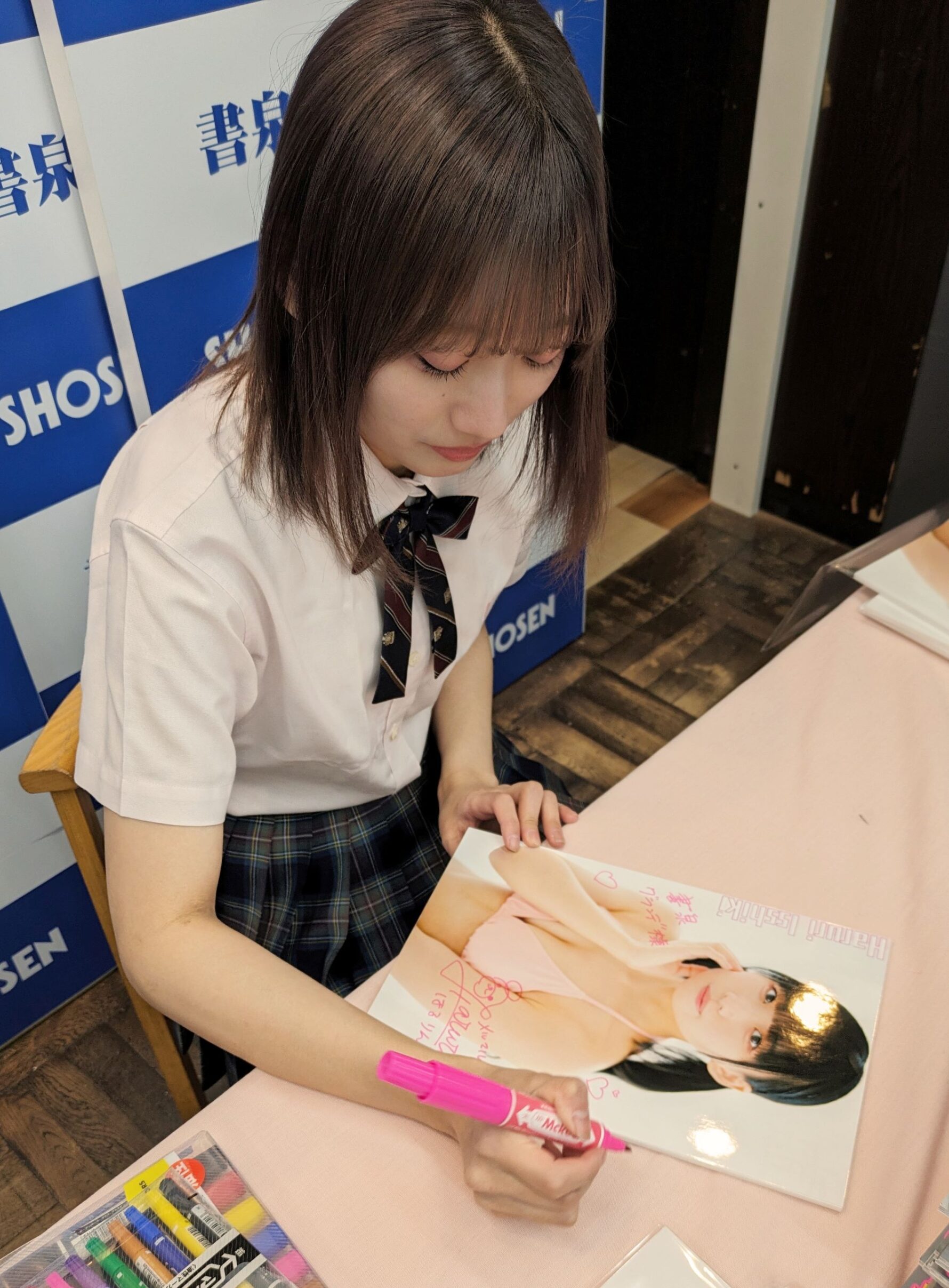【5冊券】の特典フォトパネルにサインをする一色さん。書泉グランデ用に1枚飾らせていただいております。
